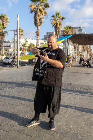 Foto de Tel Aviv, Israel - 20 de marzo de 2022, Protesta contra la agresión rusa en Ucrania. Un hombre con una bandera ucraniana en una camiseta negra con la inscripción: Israel. Mi casa está por todas partes. - Imagen libre de derechos