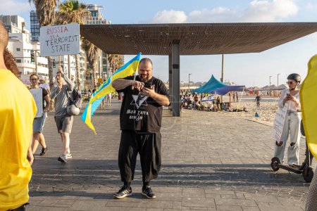 Téléchargez les photos : Tel Aviv, Israël - 20 mars 2022, Manifestation contre l'agression russe en Ukraine. Un homme avec un drapeau ukrainien dans un T-shirt noir avec l'inscription : Israël. Ma maison est partout.. - en image libre de droit