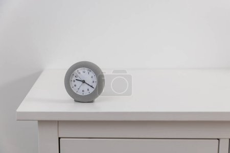 Photo for A round gray clock shows twenty past nine on a white chest of drawers. - Royalty Free Image