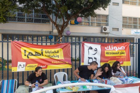 Foto de Akko, Israel - 01 de noviembre de 2022, Elecciones. Agitadores y asistentes se sientan en las mesas con boletas en frente del centro de votación. - Imagen libre de derechos