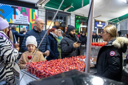 Téléchargez les photos : Londres, Royaume-Uni - Décembre 2022, La jeune fille a choisi des pommes dans le glaçage rouge. Un vendeur vendant des fraises dans des tasses à Covent Garden - en image libre de droit