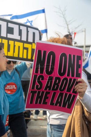 Téléchargez les photos : JERUSALEM, ISRAEL - 20 février 2023 : Manifestation israélienne près de la Knesset contre les plans du Premier ministre Benjamin Netanyahu pour piétiner la légalité. Plaque rouge - Personne n'est au-dessus de la loi - en image libre de droit