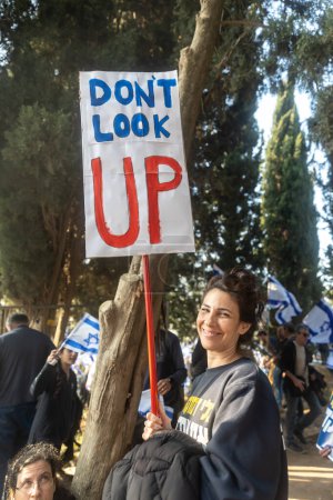 Foto de JERUSALEM, ISRAEL - 20 de febrero de 2023: Los israelíes protestan cerca de la Knesset contra los planes del primer ministro Benjamin Netanyahu de pisotear la ley. La chica con un póster - no mires hacia arriba - Imagen libre de derechos