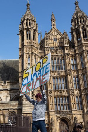 Téléchargez les photos : Londres, R.-U. 22.04.2023, The Big One Demonstration. Homme tenant une affiche - arrêter la criminalité climatique dans le contexte du parlement - en image libre de droit