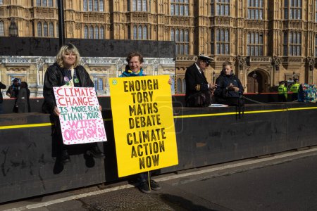 Foto de Londres, Reino Unido 22.04.2023, La gran manifestación. Man holds poster: Enough Tory math debate on climate action now. Mujer sostiene cartel: el cambio climático es más real que el orgasmo de su esposa - Imagen libre de derechos