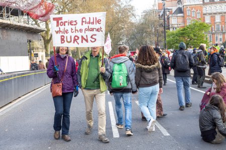 Téléchargez les photos : Londres, R.-U. 22.04.2023, The Big One Demonstration. Homme et femme tiennent une affiche - violon tory pendant que la planète brûle - en image libre de droit