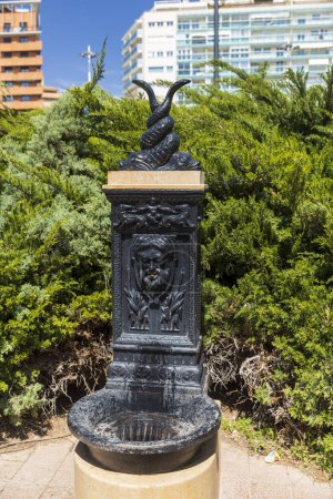 Valencia, Spanien - 20. April 2024, Ein Trinkbrunnen in einem Park aus schwarzem Metall in Form eines Satyrs, der einen Wasserstrahl aus seinem Mund ablässt.
