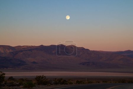 Einsame kalifornische Landschaft mit Vollmond am frühen Morgen kurz vor Sonnenaufgang über den Bergen, Roadtrip durch typische südwestamerikanische Wüste, Death Valley, USA