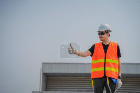 Photo for Asian engineers wearing protective vest and white hardhat standing thumb ups to the copy space while holding tablet. - Royalty Free Image