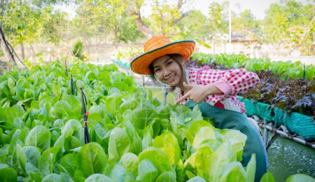 Photo for Beautiful asian female farmer introduces her organic vegetables by pointing in organic vegetable garden. - Royalty Free Image