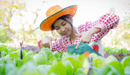 Photo for Beautiful asian female farmer joyfully introduces her organic vegetables in organic vegetable garden. - Royalty Free Image