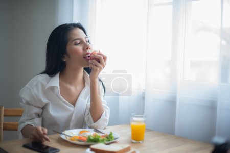 Téléchargez les photos : Belle femme asiatique mangeant une pomme et sur la table prenant le petit déjeuner et un verre de jus. - en image libre de droit