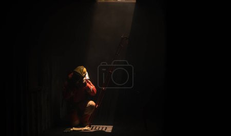 Téléchargez les photos : Le pompier est assis à côté d'une échelle rouge dans une pièce sombre une lumière douce brillait d'en haut. - en image libre de droit