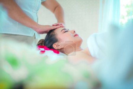 Foto de Vista lateral de la masajista profesional es hábilmente dando un masaje a base de hierbas en una cómoda cama rociada con pétalos de rosa. - Imagen libre de derechos