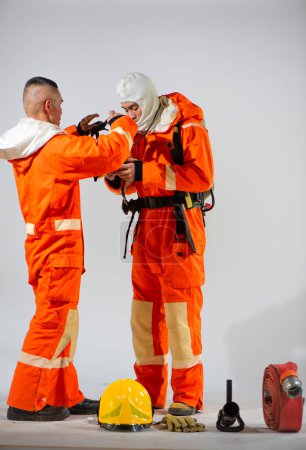 Téléchargez les photos : Pompier professionnel se prépare à enfiler un masque pour son partenaire assurant leur sécurité dans l'exercice de leurs fonctions sur un fond blanc. - en image libre de droit