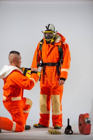 Téléchargez les photos : Pompier professionnel agenouillé vérifie la pertinence d'un casque jaune avant de le porter à son partenaire. - en image libre de droit