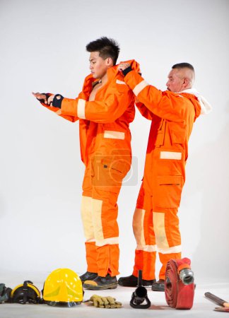 Téléchargez les photos : Pompiers professionnels portant l'uniforme tandis que son partenaire a aidé sur un fond blanc. - en image libre de droit