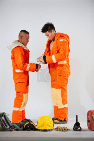 Téléchargez les photos : Pompier professionnel aidant la main à leur partenaire les aider à enlever leur uniforme avec soin sur fond blanc. - en image libre de droit