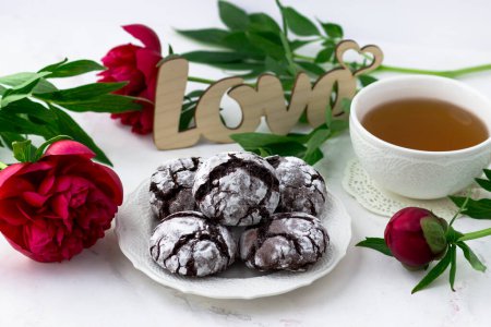 Foto de Golosinas en una mesa blanca. Galletas de chocolate, una taza de té y peonías - Imagen libre de derechos