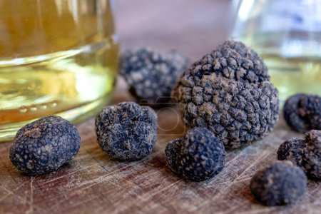 Photo for Freshly picked black truffle mushrooms on a wooden plate with a bottle of white wine in the background. - Royalty Free Image