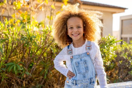Photo for Portrait of beautiful smiling little girl with curly hair close up, against background of summer city park. - Royalty Free Image