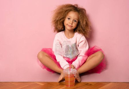 Little african american child girl drinking orange juice,isolated on pink background