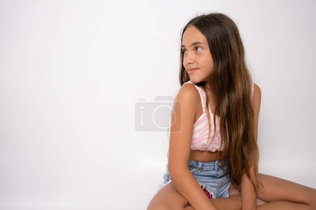 Photo for Young 11 year old girl sit on floor rest with a smile into camera with copy space isolated on white - Royalty Free Image