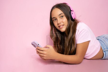 Foto de Chica joven acostada en el suelo y el uso de teléfono inteligente aislado sobre fondo rosa. - Imagen libre de derechos