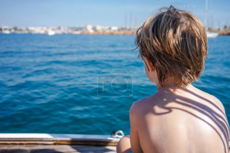 Téléchargez les photos : Vue arrière du petit garçon assis sur un voilier - en image libre de droit