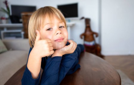 Photo for The boy lies on the table showing thumb up. The emotions of a child. Portrait. - Royalty Free Image