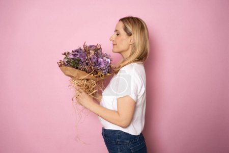 Foto de Hermosa joven rubia sosteniendo flores aisladas sobre fondo rosa. - Imagen libre de derechos