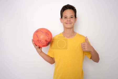 Foto de Sonriente adolescente chico en ropa deportiva celebración pelota de fútbol mostrando pulgar hacia arriba - Imagen libre de derechos