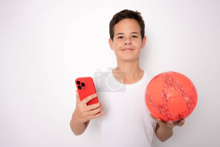Téléchargez les photos : Sourire adolescent garçon en vêtements de sport tenant ballon de football et smartphone - en image libre de droit