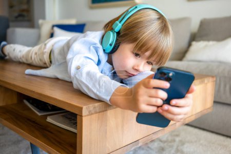 Adorable caucasian child boy boy using smartphone lying on a table at home
