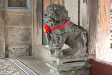 Une majestueuse sculpture de tigre gardien ornée d'un ruban rouge au temple Thian Hock Keng