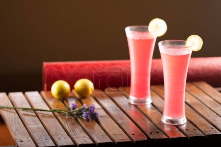 Zwei Gläser erfrischende rote Cocktails mit Limettenscheiben auf einem Holztisch.