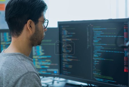 Téléchargez les photos : Asiatique invite ingénieur développeur codage app avec des données logicielles assis devant moniteur d'ordinateur au bureau - en image libre de droit