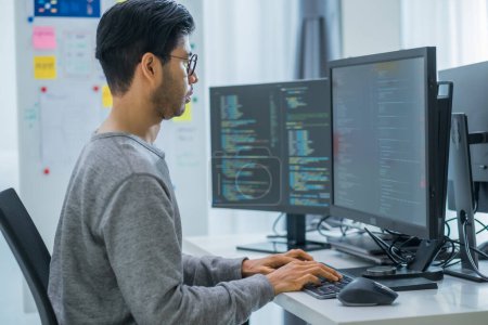 Téléchargez les photos : Asiatique invite ingénieur développeur codage app avec des données logicielles assis devant moniteur d'ordinateur au bureau - en image libre de droit