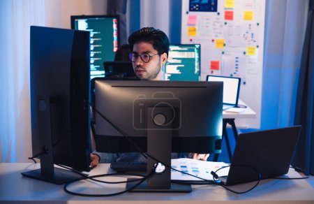 Téléchargez les photos : Développeurs de logiciels asiatiques travaillant sur plusieurs écrans affichant le code et les diagrammes d'application la nuit dans le bureau moderne - en image libre de droit