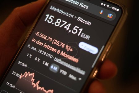Téléchargez les photos : The hand of a man holding a mobile phone and checking the Bitcoin course - Falling courses - Google Chrome search, Radolfzell am Bodensee, January 9th, 2023 - en image libre de droit