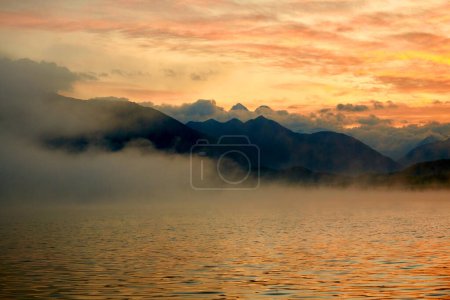 Photo for Atmospheric morning fog over Lake Yazevoe in eastern Kazakhstan. Lake Yazevoe is located at an altitude of 1685 meters above sea level. It is part of the State National Natural Park "Katon-Karagay".  Dawn over the foggy lake. Blur effect. - Royalty Free Image