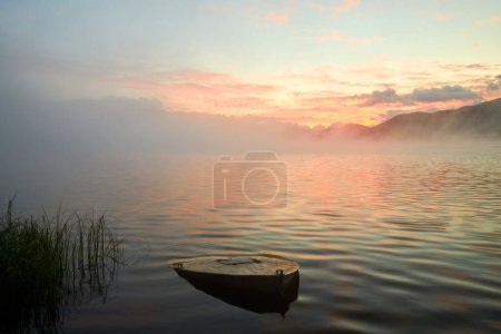 Téléchargez les photos : Brouillard atmosphérique matinal sur le lac Yazevoe dans l'est du Kazakhstan. Le lac Yazevoe est situé à une altitude de 1685 mètres au-dessus du niveau de la mer. Il fait partie du Parc Naturel National de l'État "Katon-Karagay". Un bateau coulé au premier plan. Effet flou. - en image libre de droit