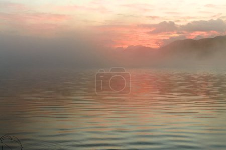 Téléchargez les photos : Brouillard atmosphérique matinal au-dessus du lac Yazevoe dans l'est du Kazakhstan. Lac Yazevoe est situé à une altitude de 1685 mètres au-dessus du niveau de la mer. Il fait partie du Parc Naturel National de l'État "Katon-Karagay". Aube au-dessus du lac brumeux. Effet flou. - en image libre de droit