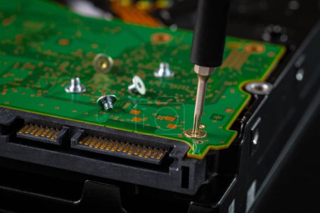 Festplatte und Leiterplatte mit SATA-Stromanschluss. Magnettreiber Torx-Bit und kleine Maschinenschraube auf dunklem Hintergrund.