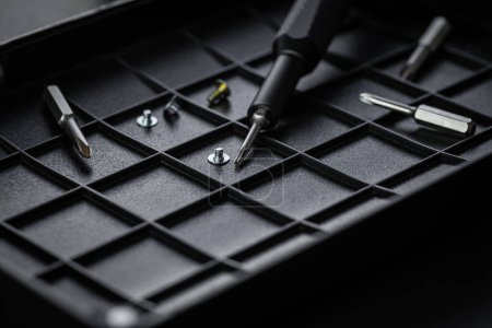 Torx-Laufwerk-Bit und Aluminium-Bit-Treiber auf schwarzem Sortierfach. Schrauben und Antriebsmeißel verstreut. Schraubendreher-Griff mit magnetischer Bit-Buchse und Rändelgriff.