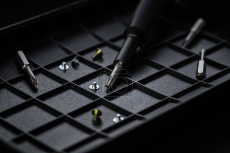 Torx drive bit and aluminum bit driver on black sorting tray. Screws and drive bits scattered around. Screwdriver handle with magnetic bit socket and knurled grip.