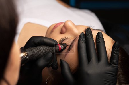 Photo for Closeup shot of a cosmetician in gloves making permanent brow makeup to a young woman at beauty salon - Royalty Free Image