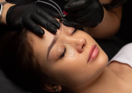 Téléchargez les photos : Vue du dessus d'un cosmétique faisant du maquillage permanent pour une femme au salon de beauté - en image libre de droit