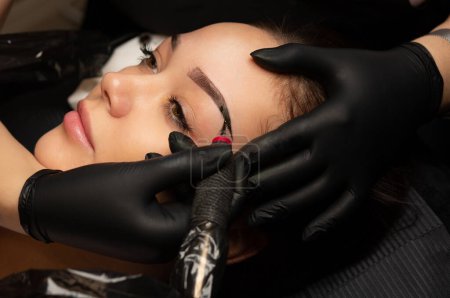 Photo for Lovely brunette woman undergoing procedure of permanent brow makeup in tattoo salon. Closeup top view - Royalty Free Image