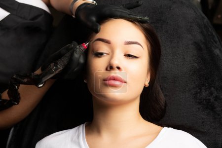 Téléchargez les photos : Magnifique femme subissant une procédure de maquillage permanent des sourcils en poudre dans le salon de tatouage. Vue du dessus - en image libre de droit